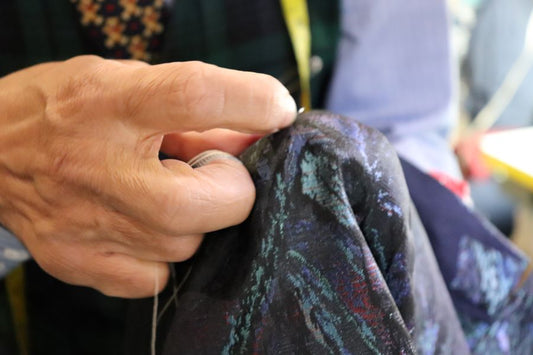  Close-up macro shot of artisanal hand-stitching on a suit jacket. A needle and thread secure a silk lining to a horsehair canvas. The focus is on the precision of the hand-tacking stitches used in traditional West End tailoring.
