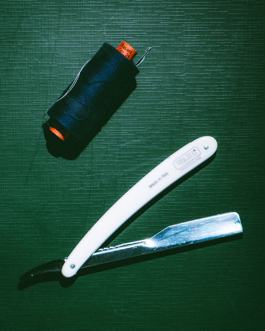 Close-up of a master tailor's needle thread alongside classic barber tools on a wooden workbench, representing the Blade and Thread collaboration between West End Tailor and Kolanamara Barber Shop in Brisbane. 