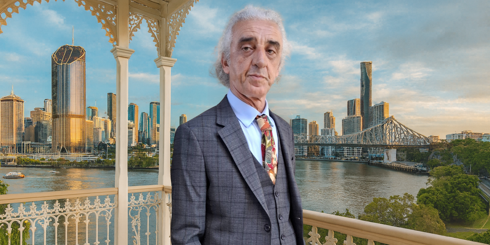 Man in a suit standing in front of the Brisbane city skyline with a bridge and river.